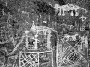 Ancient cave wall with white pictographs of people, animals, and geometric shapes on rough rock surface.
