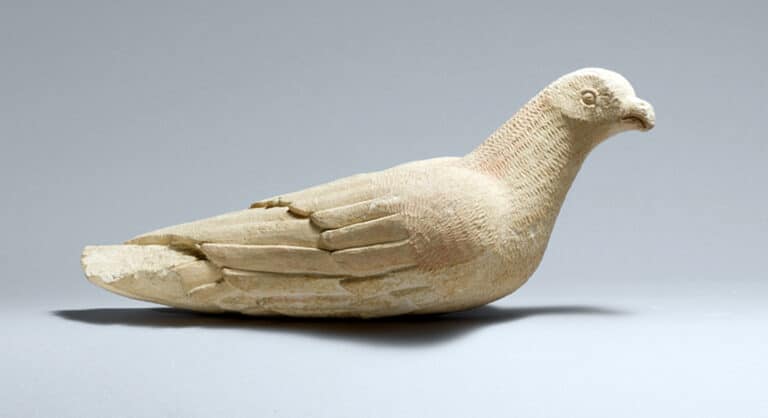 Beige stone sculpture of a resting dove on a gray background.