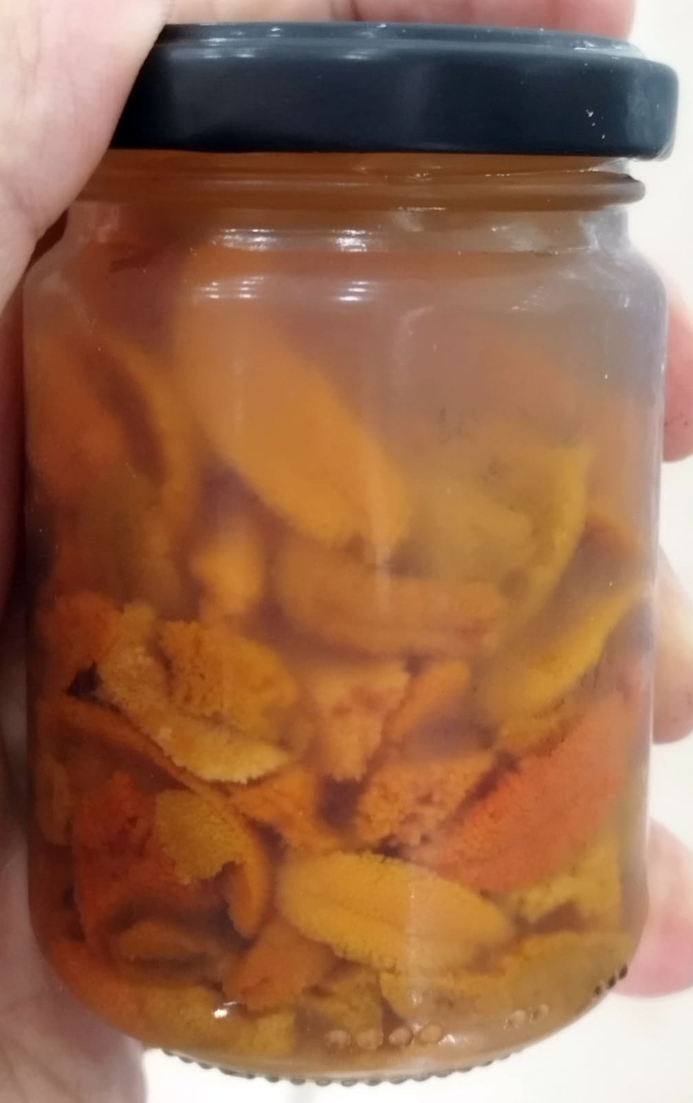 Jar of orange fruit jam with chunky pieces, held by a hand in frame.