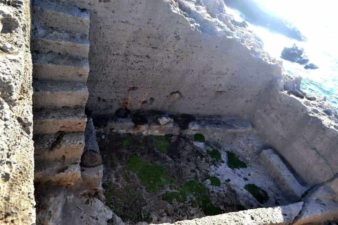 Old stone stairwell and crumbling walls by the shore, with mossy ground and seawater nearby.