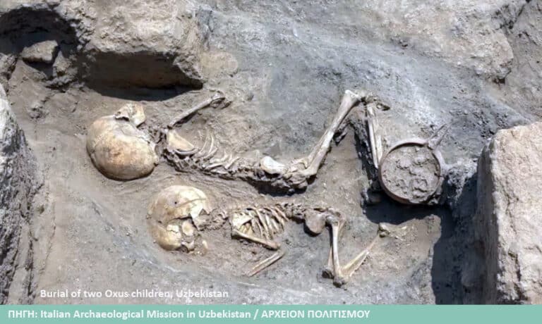 Two ancient child skeletons buried in a shallow grave in Uzbekistan, with a clay vessel nearby and surrounding soil.