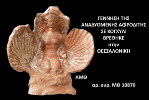 Terracotta sculpture of a baby Aphrodite inside a large seashell, set against a black background with Greek exhibit text (found in Thessaloniki, catalog MO 10870).