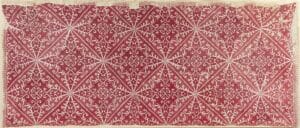 Rectangular textile with a red background and white geometric diamond motifs repeating in a grid across the fabric edge-to-edge.