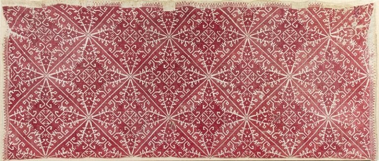 Rectangular textile with a red background and white geometric diamond motifs repeating in a grid across the fabric edge-to-edge.