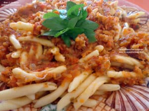 Pasta with a chunky tomato-meat sauce and a sprig of fresh basil on top.