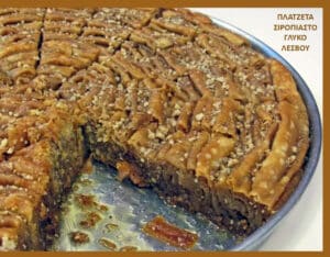Traditional syrup-soaked pastry from Lesvos in a round pan, sliced with a dense, nutty filling and sesame topping, one piece removed.