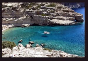 Small white boat floating in a turquoise cove surrounded by rocky cliffs and clear blue water.