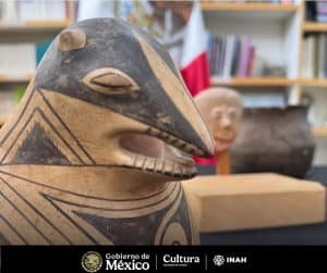 Close-up of a black and beige carved figure with geometric patterns, on display with bookshelves in the background.