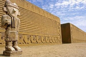 Terracotta warrior statue in front of a long carved clay wall with rows of figures