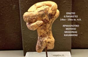 Ancient stone figurine on display with Greek museum text visible on the right, referencing a Kalamata archaeology exhibit.