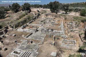 Ruins of the Temple of Apollo at Gortyn: stone foundations, scattered blocks, and a few visitors resting among the ancient ruins under a blue sky.