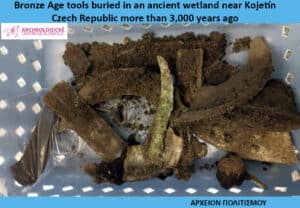 Bronze Age tools unearthed from an ancient wetland, with several corroded bronze fragments in a light blue basket and a small logo in the corner.