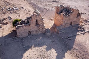 Desert ruins with two stone towers and scattered rubble, casting long shadows on the ground.