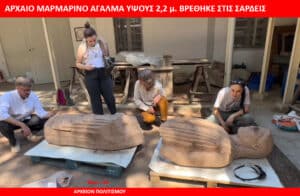 Group of researchers examining two large carved stone fragments outdoors under a red banner for context or news report reframing the scene as an archaeological work site.