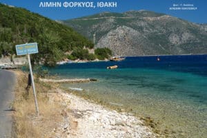 Coastal scene at Port of Phorcys with clear turquoise sea, green hills, and a small boat near the rocky shore.