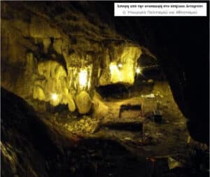 Cave interior with stalactites and stalagmites, illuminated by yellow lights, and an excavation area with tools.