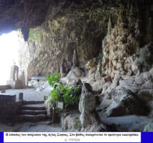 Interior of a rocky cave with a small stone chapel and steps leading to an arched entrance bathed in daylight outside.