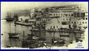Historic harbor scene of Chania (Crete) with moored ships and a row of old stone buildings along the quay; caption notes XANIA LIMANI PERI TO 1890.
