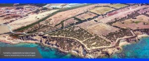 Aerial view of the Kamarina promontory: cliffed coastline, turquoise sea, and terraced fields with olive trees.