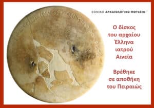 Round ancient Greek medical disk with visible cracks; Greek inscription and a museum label on white background, indicating it was found in a Piraeus warehouse.